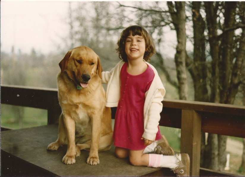 Danielle at five, kneeling with her dog. She's wearing AFOs and Velcro shoes.